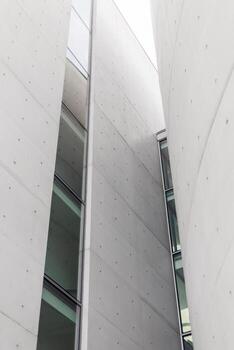 Tall concrete structures with large glass windows create a modern urban environment. The design showcases sharp lines and minimalistic features under a cloudy sky photo