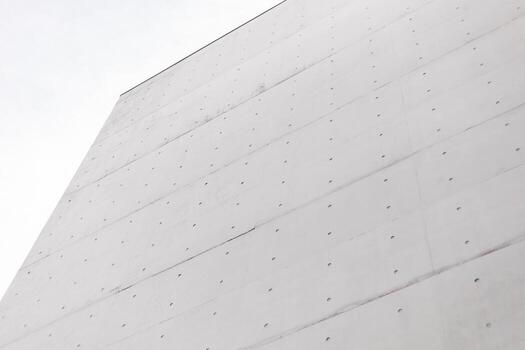 A large white concrete wall displays a minimalist design with visible dots and a smooth surface. The cloudy sky above adds a serene atmosphere to the contemporary setting photo