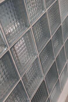 A wall made of clear glass blocks featuring geometric patterns reflects light and adds texture, enhancing a contemporary space with its unique design photo