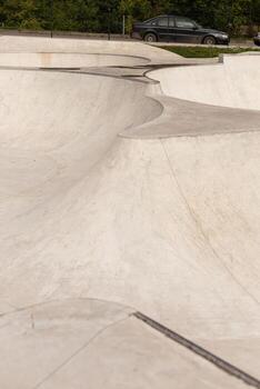 The skatepark features smooth concrete curves and ramps, inviting skaters to practice tricks. A parked car is visible in the background, enhancing the urban setting photo