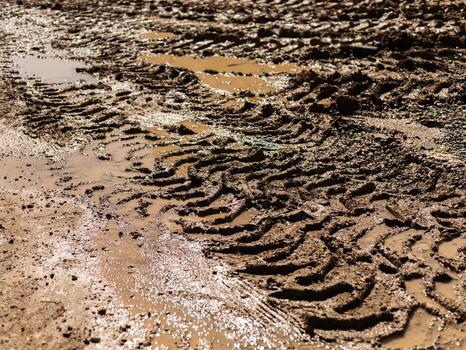 Tire tracks create intricate patterns in wet mud at a rural construction site. Puddles form in the low areas, reflecting the sky. The scene highlights the effects of rain on the terrain photo