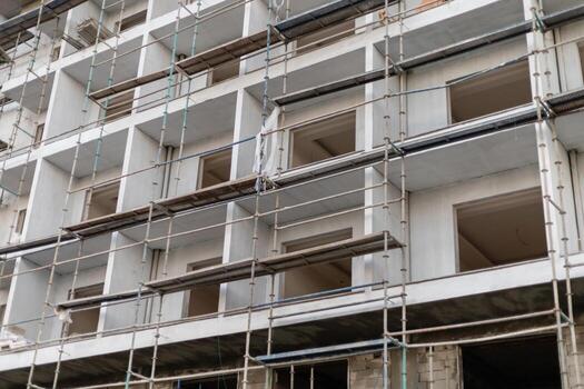 Construction workers are busy at a modern building site where scaffolding surrounds unfinished walls with open window frames, indicating active development in a city area photo