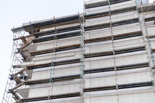 Workers are busy on scaffolding while renovating a tall building in an urban environment. The construction site is bustling with activity as crews manage various tasks photo
