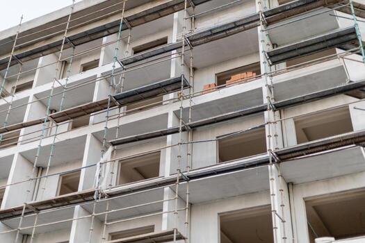 Workers are using scaffolding to access different levels of a multi-story building under construction. The image shows exposed walls and construction materials nearby photo