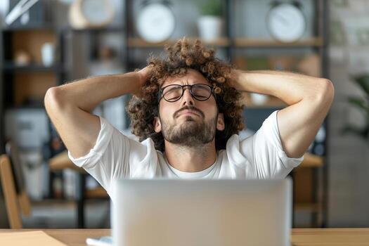 An adult is sitting at a desk in a cozy workspace, taking a break from computer work. He is practicing breathing exercises, showing a focused expression as he relaxes and manages stress photo