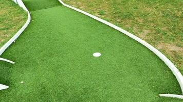 mini golf traccia con buco e bianca rotaie su artificiale torba nel un' parco, telecamera movimento lungo il corso. orizzontale telaio, pulito B rotolo con copia spazio, nessuno. video