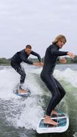 dynamisk surfing duo navigerande vågor i elegant svart våtdräkter, visa upp skicklighet och precision på slät vattnen under mulen himmel video