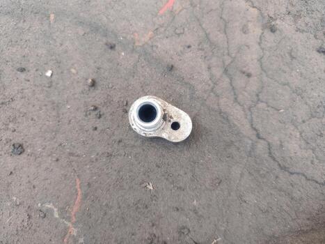 Small metallic part lying on dusty ground, minimal mechanical composition, industrial workshop background, single hardware element detail, closeup engineering texture, construction material. photo