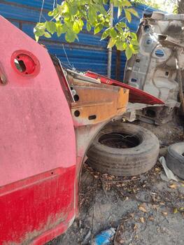 Old red vehicle rear section with exposed metal structure, junkyard automotive part, industrial repair setting, mechanical framework, engineering element, weathered corrosion texture. photo