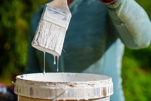 A painter s workspace features a brush loaded with white paint, dripping into an open container, ideal for showcasing DIY projects, home improvement, or design concepts. photo