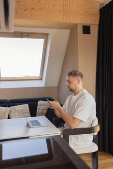 Man using smartphone while working with laptop at home office. Concept of remote work, online communication, fintech, digital banking, e-commerce, productivity and technology photo