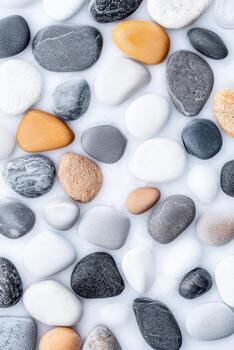 Smooth pebbles lie scattered on a soft white surface. Various rounded stones display natural colors and textures. Peaceful arrangement of earth toned elements. Close up view. photo