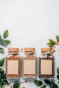 Glass jars holding granules aligned against white surface with fresh leaves surrounding rustic bottles and blank labels attached for text photo