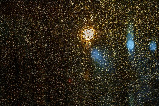 An abstract background of raindrops on glass at night with a golden bokeh effect. Blurred city lighting through the wet window creates a moody and atmospheric texture. photo