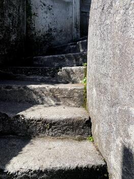 Old weathered concrete stairs winding upwards, rugged texture with moss and small plants growing along the stone walls and steps. Decorative background for design photo