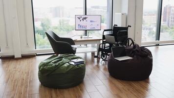 innovativ kontor miljö med rullstol tillgänglighet, bekväm böna påsar, och teknologi verktyg placerad i främre av stor fönster med stad se video