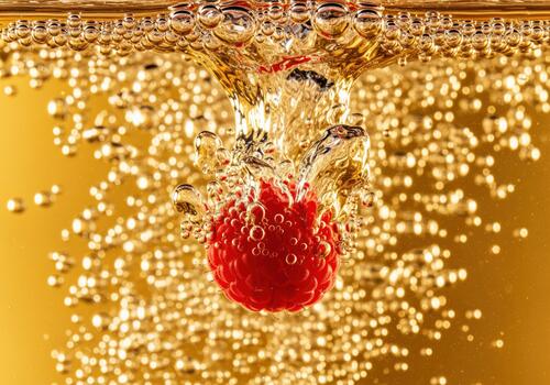 Dynamic close up of a red raspberry sinking into effervescent golden drink photo