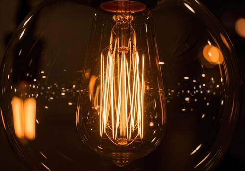 A close up macro shot of a glowing vintage edison light bulb filament creating warm amber light photo