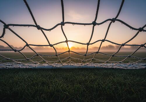 Atmospheric view through a soccer net covered in dew drops during foggy sunrise. photo