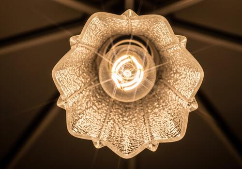 Warm glowing filament bulb viewed from below inside a decorative glass lamp shade. photo