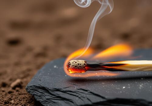 Burning matchstick with bright flame and smoke resting on dark slate close up macro photo