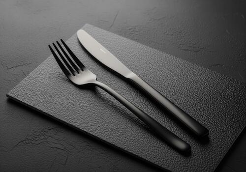 Elegant matte black fork and knife cutlery set resting on a dark textured slate photo