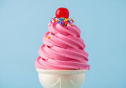Luscious pink soft serve ice cream cone topped with colorful sprinkles and a cherry. photo
