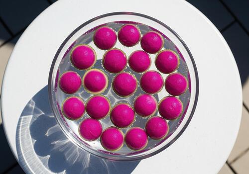 Overhead view of bright magenta spheres floating in water in a glass bowl on a white table. photo