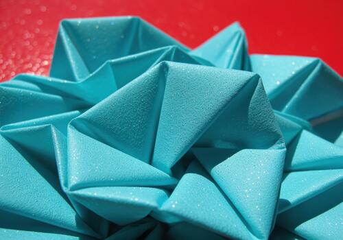 Close up of sparkling turquoise paper folded into sharp geometric origami pattern on red photo