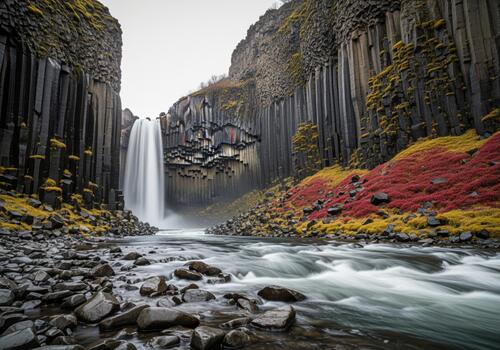 Powerful waterfall cascading down dark hexagonal basalt columns into a rocky river photo