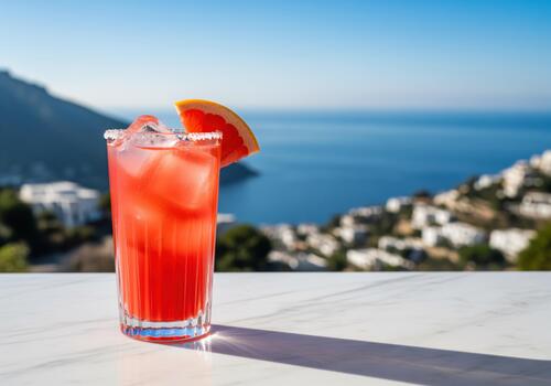 Sparkling ruby red paloma cocktail with ice and grapefruit wedge on a marble table overlooking the sea. photo