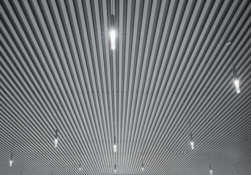 Monochromatic low angle view of a modern architectural ceiling with parallel metal slats and bright pendant lights photo