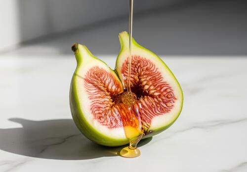 Honey dripping onto a fresh green fig sliced in half on a marble surface photo