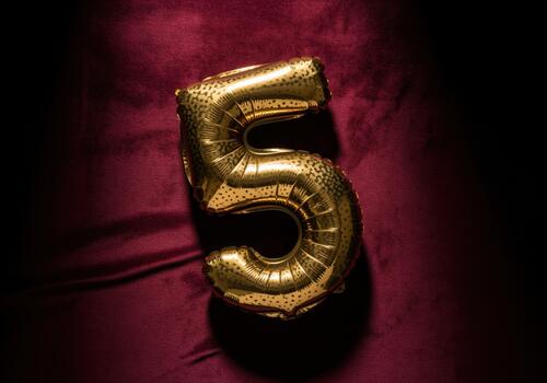 Luxurious gold number five foil balloon resting on dark red velvet fabric photo