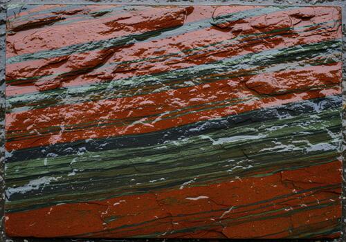 Glistening stratified rock surface texture featuring vibrant rust red and deep green layers photo