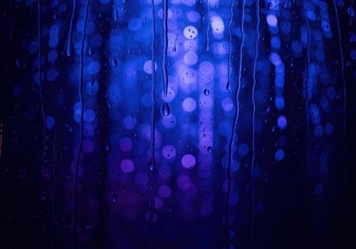 Deep blue and purple bokeh background with raindrops streaming down wet glass photo