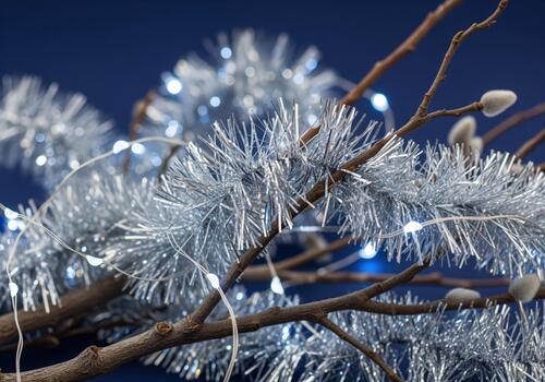 Shimmering silver tinsel and glowing string lights decorating dry winter branches photo