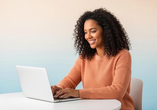 Cheerful young black woman typing on a laptop computer while sitting at a table. photo