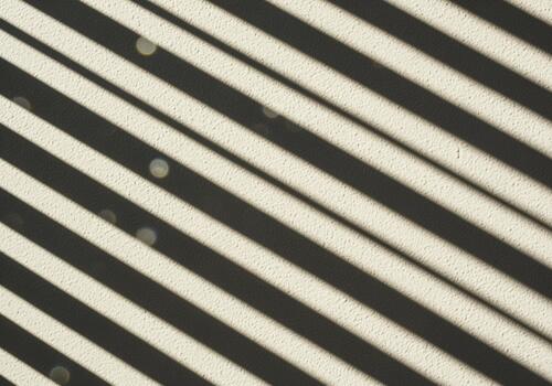 Diagonal striped shadows from venetian blinds cast on a textured stucco wall photo