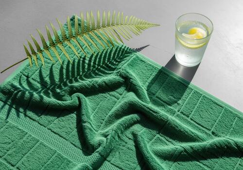 Plush green towel with geometric pattern, fern shadow, and refreshing lemon water. photo
