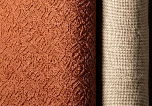 Close up of two contrasting fabric rolls, textured orange diamond pattern and natural beige textile. photo