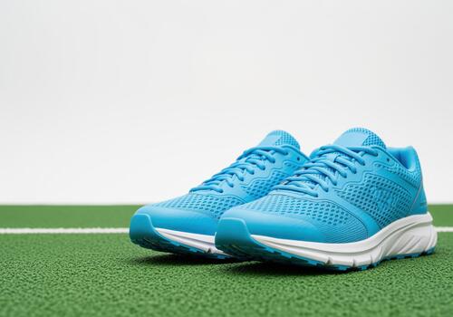 Bright sky blue athletic running shoe pair resting on green artificial turf field photo