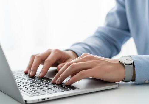 Professional hands typing on a modern laptop keyboard, wearing a stylish wristwatch. photo