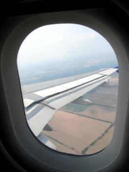 View From a Plane Porthole Showcasing the Wing Above Sprawling Agricultural Fields Below photo