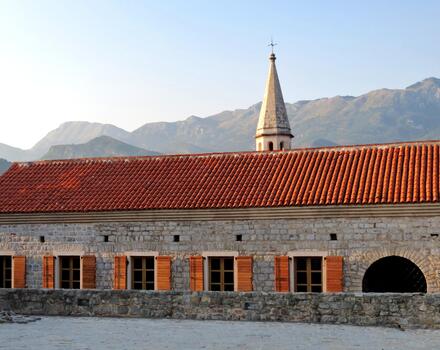 Old stone building with shuttered windows. Bell tower and mountains in the background photo