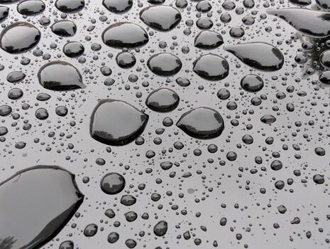 Raindrops create a shimmering pattern on a black surface in a quiet outdoor setting during a cloudy day photo