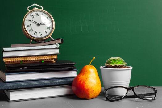 Study setup with books, clock, glasses, and pear on a desk in a classroom setting photo