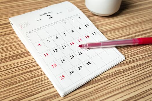 Calendar showing February days with a red pen resting on the side in a cozy setting photo