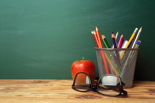 Tools for learning are arranged on a wooden desk with a chalkboard in the background photo