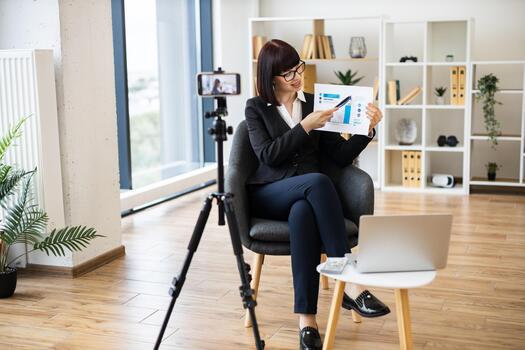 Caucasian woman presenting business analytics on camera through blogging using report and statistics chart. photo
